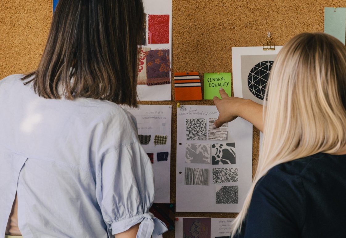 2 female trend forecasters working on a DEI forecast on a corkboard wall with fabrics and colour palettes